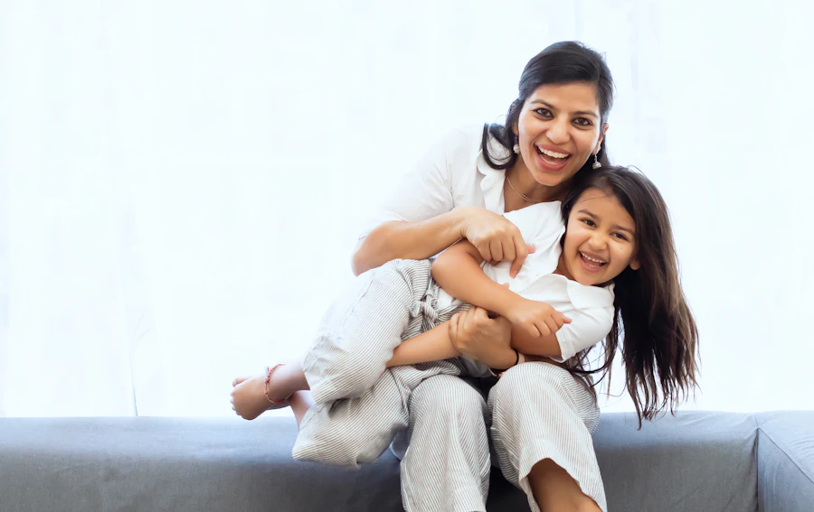 Smiling mother hugging her laughing daughter on a sofa at home